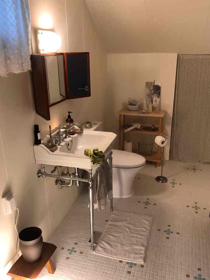 白い壁と勾配天井が特徴の小さなトイレ、木製棚とバスマットが配置された居心地の良い空間