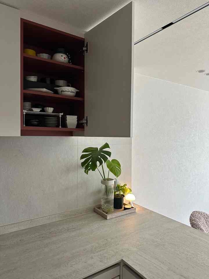 ライトグレーの壁とセラミックカウンター、赤い内側の上部キャビネットが配置されたシンプルでモダンなキッチンの空間