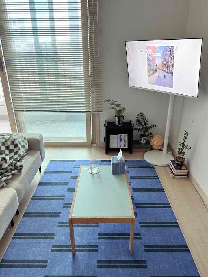 青いラグと白い家具が配置されたモダンなリビングルーム、大きな窓のそばで明るく清潔な雰囲気のインテリア