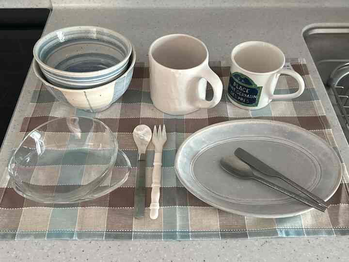 パステル調チェック柄のテーブルクロス上にスカイブルーの食器、透明なガラスボウル、マグカップが配置されたキッチンスペース