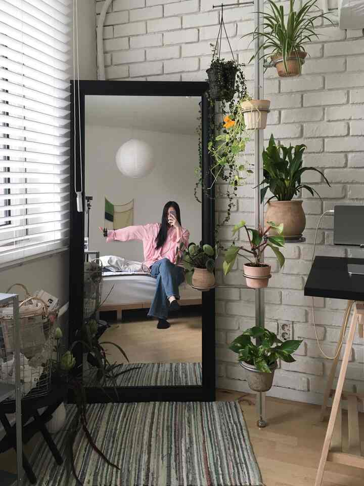 白と木目調の寝室、巨大な全身鏡と複数の植物が自然な雰囲気を演出するインテリア