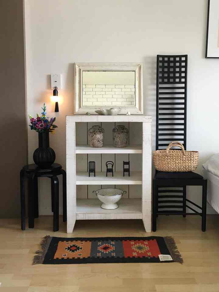 ナチュラルな雰囲気のヴィンテージホワイトの棚とブラックのスツール、チェアが配置された寝室の入口スペース