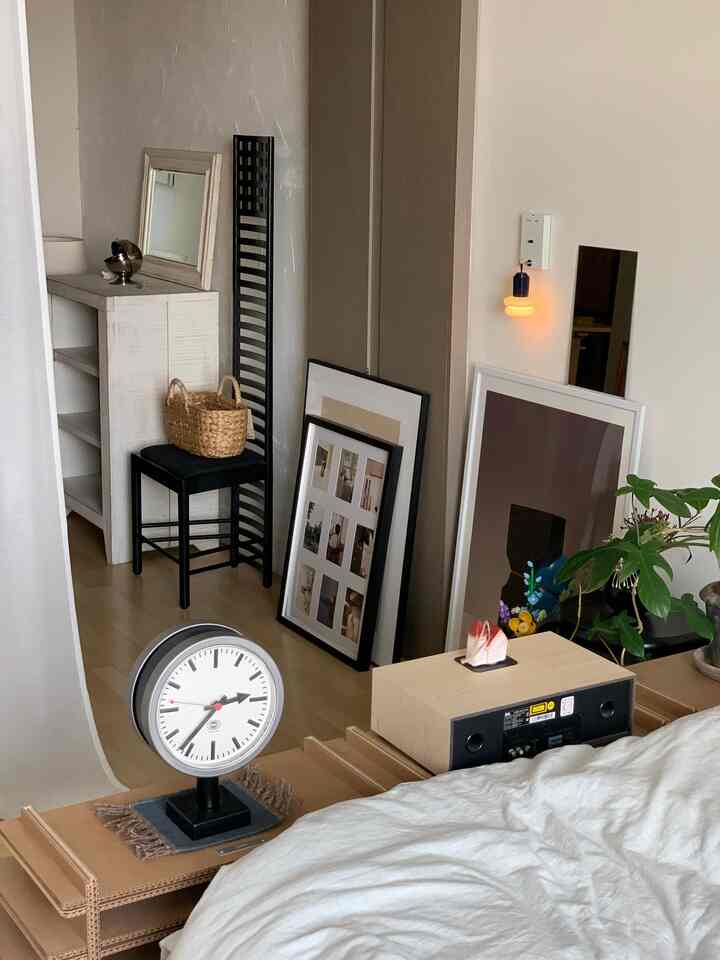 白い壁とナチュラルウッドの床がある寝室、床に額縁と鏡がラフに置かれたシンプルなインテリア