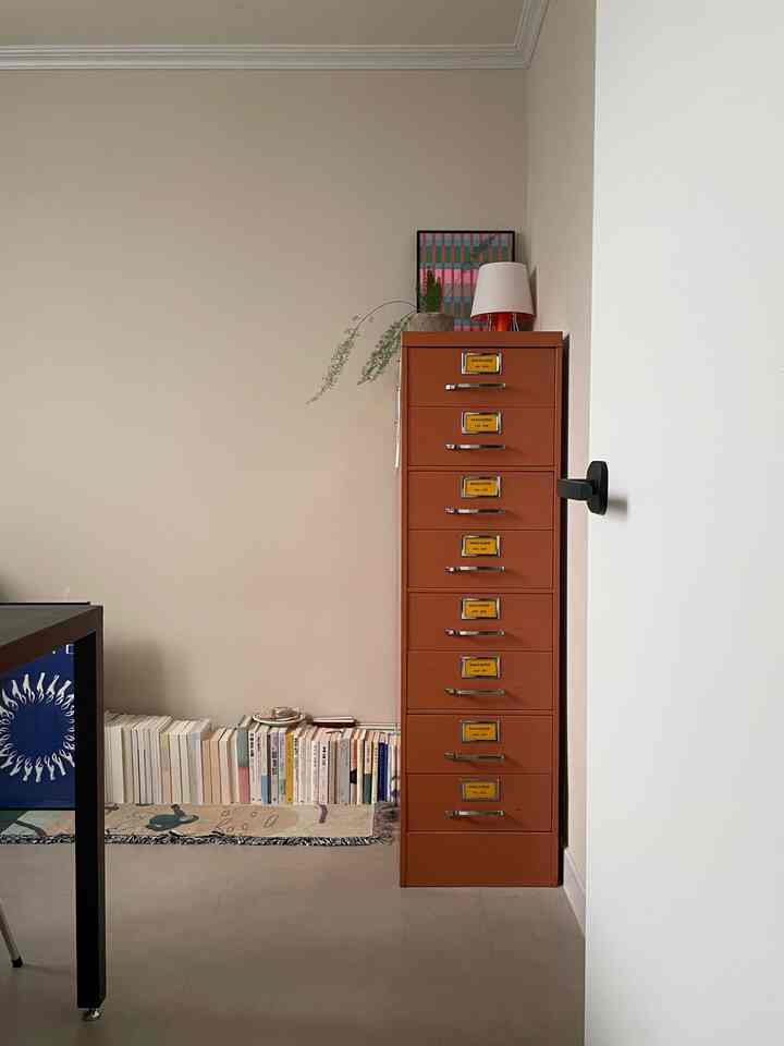 ブラウン調のリビング、右側にオレンジのキャビネットがあり、床に整頓された本が並ぶシンプルで落ち着いた雰囲気のインテリア