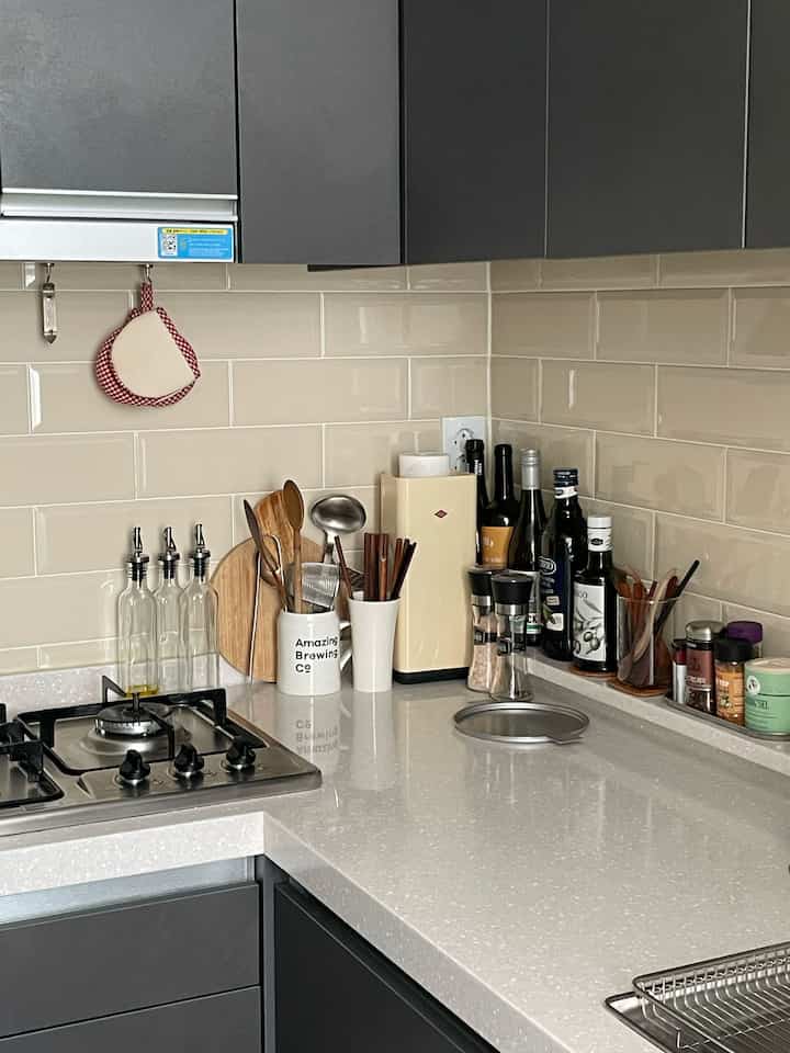 ベージュのタイルとグレーの収納が配置されたナチュラルカラーのキッチン、調理器具やまな板が整頓された雰囲気のあるインテリア