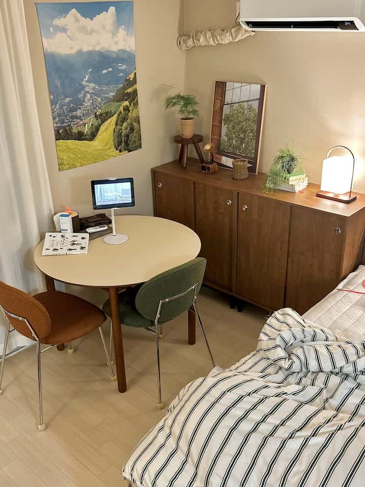 ベージュと木目調の色合いが調和したコンパクトな寝室、丸テーブルと椅子が配置された暖かみのある空間