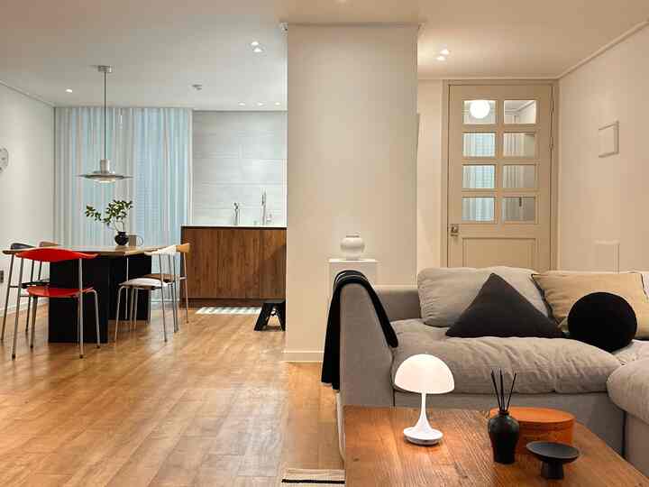 白い壁と木目調の床が調和する4人用のリビング兼ダイニングルーム、モダンなソファとテーブルランプで雰囲気のある空間