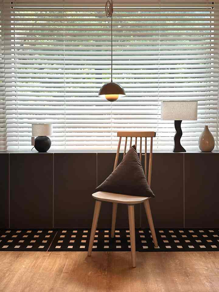 チャコールと木目調のリビング、三角形クッションが置かれた木製チェアと実用的な収納が配置されたシンプルモダンなインテリア