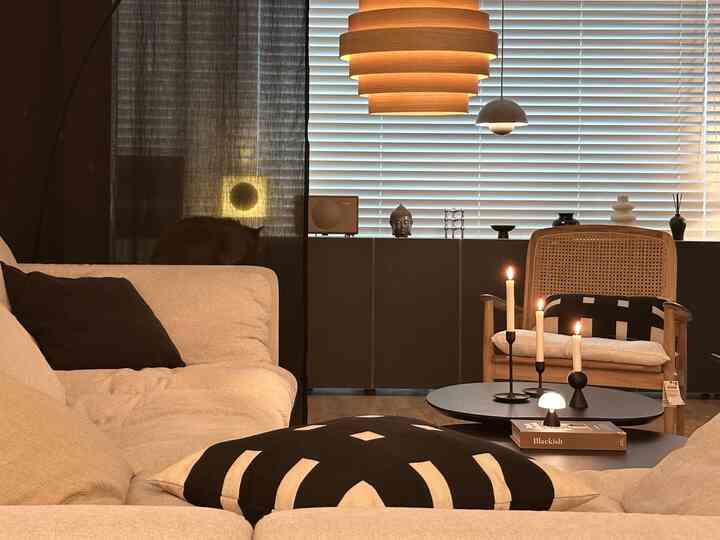 ナチュラルカラーとブラックが調和したリビング、ベージュのソファとラタンのアームチェア、キャンドルと木製のシャンデリアが配置された温かみのあるインテリア