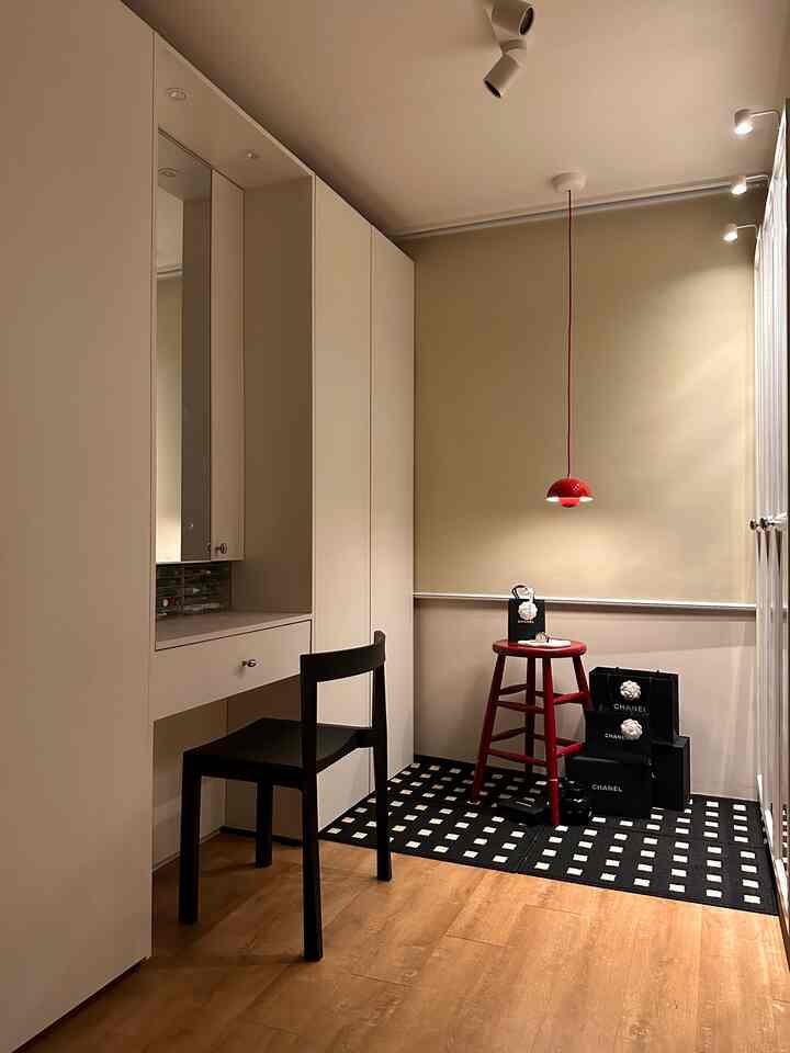 ホワイトとブラウンのモダンなウォークインクローゼット、オーダーメイドの収納と赤いスツールが配置された整った空間