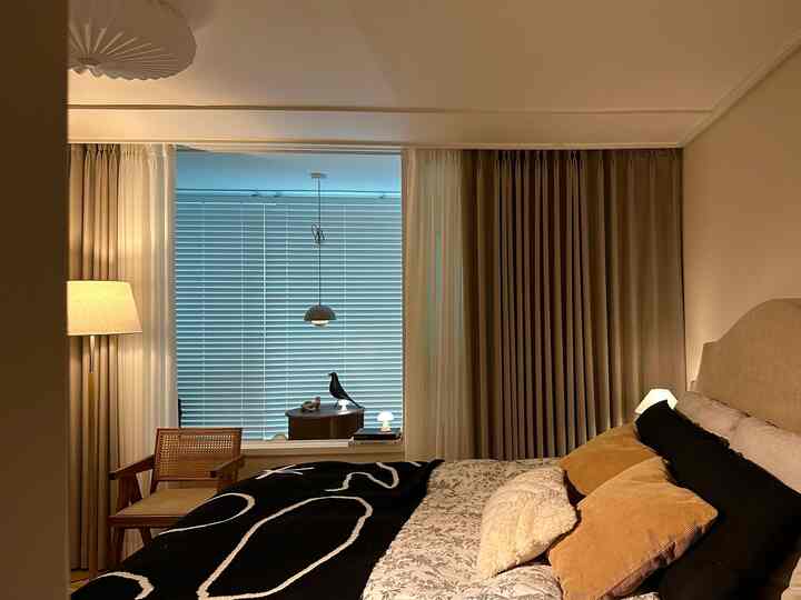 ベージュとブラウンの色調の寝室、ベッド、アームチェア、カーテンが配置された雰囲気のあるインテリア