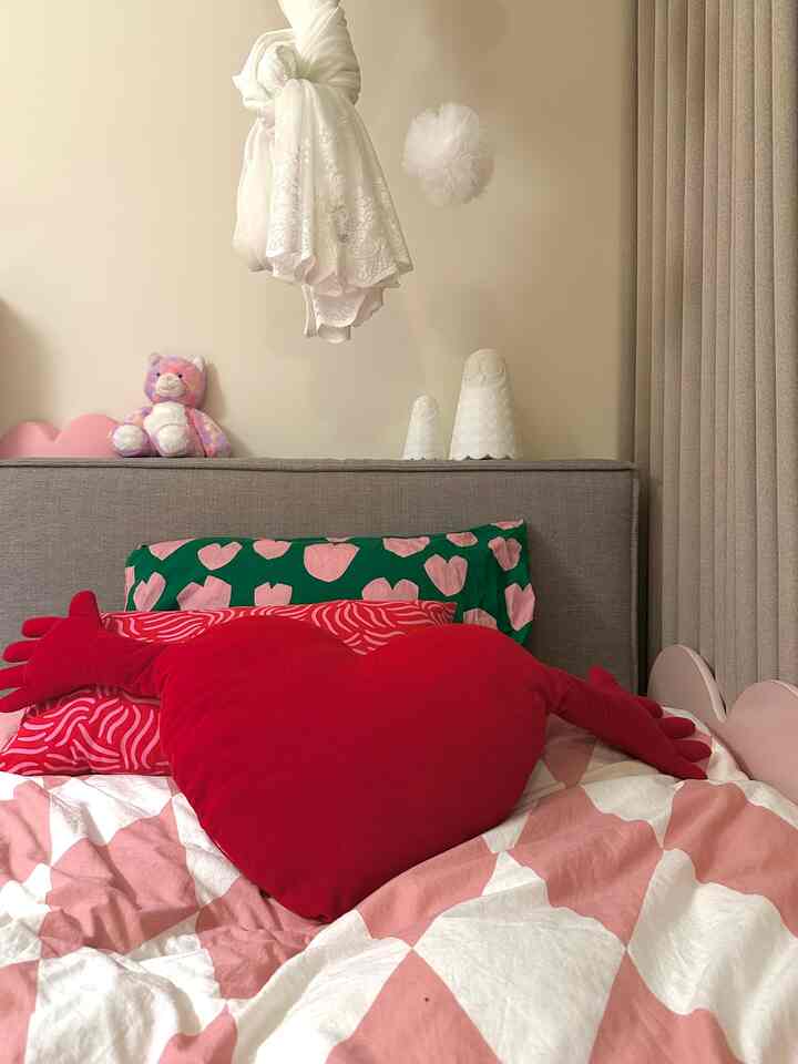 ピンクとレッドの色調が特徴的な子供部屋、ハート形クッションとぬいぐるみが配置された温かみのあるインテリア