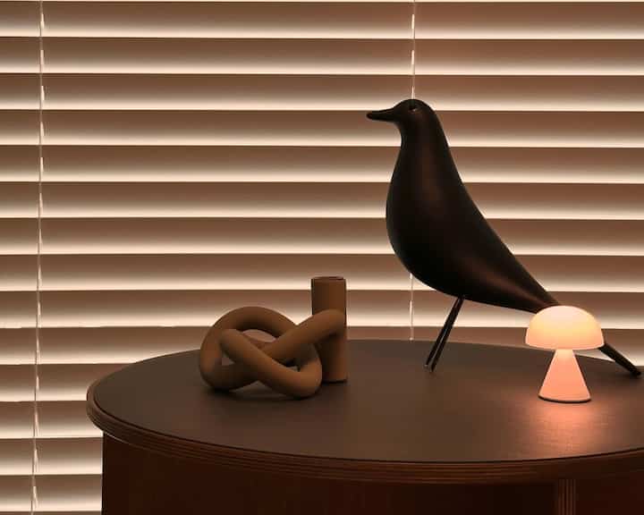 ウッドトーンとブラウンのサイドテーブルに、灯りのついたテーブルランプと鳥のオブジェが配置された、雰囲気のあるおうちカフェ空間