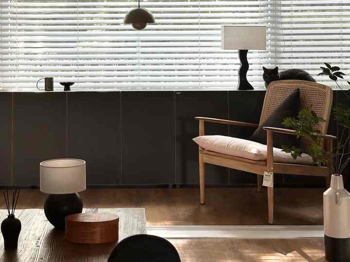 ウッドトーンの床とモダンナチュラルスタイルのリビング、黒い収納キャビネットとオブジェ、白いブラインドが配置された雰囲気のある空間