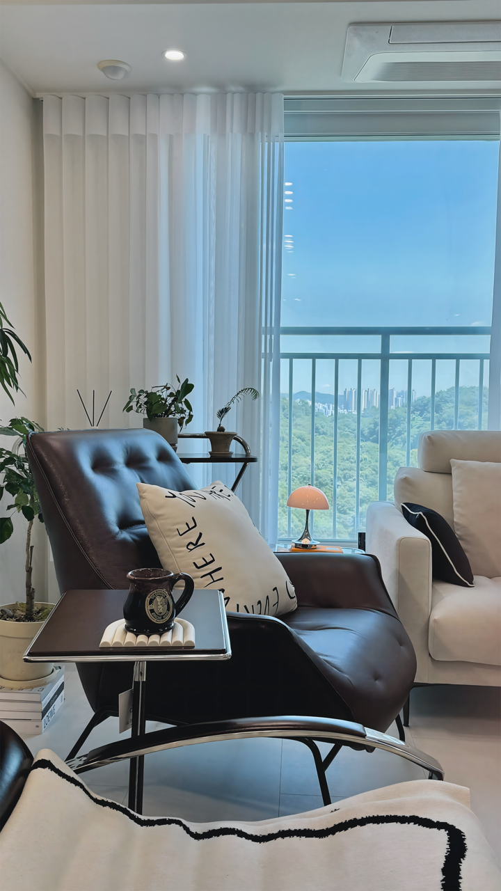 スカイブルーの空色と白いカーテン、ソファ、ブラウンのアームチェアが配された、バルコニーの見えるリビングルーム