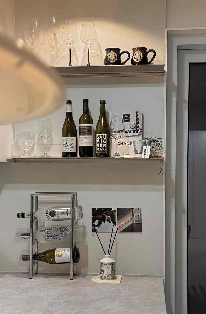 ホワイトとグレーの色調のキッチン、棚とワインラックにワイングラスやオブジェが配置されたミニマルな雰囲気のインテリア