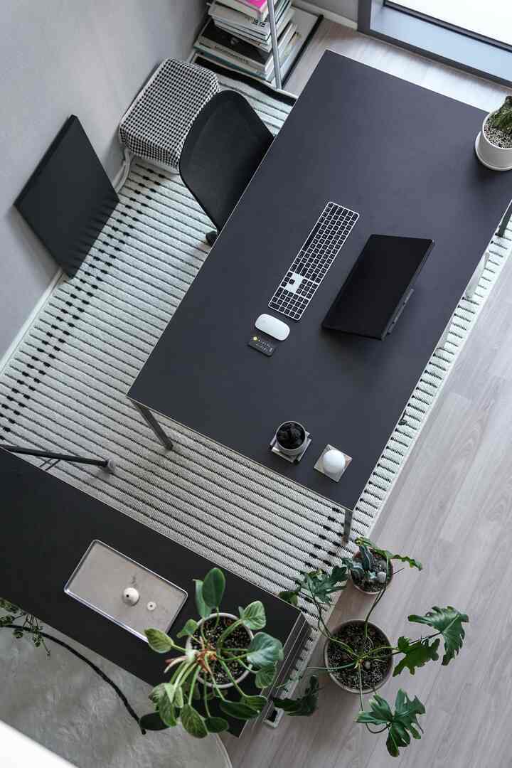 ホワイトとブラックのトーンで統一されたモダンなホームオフィス、黒いデスクとメッシュチェアにデジタル機器が整頓され、観葉植物が配置された印象的な空間