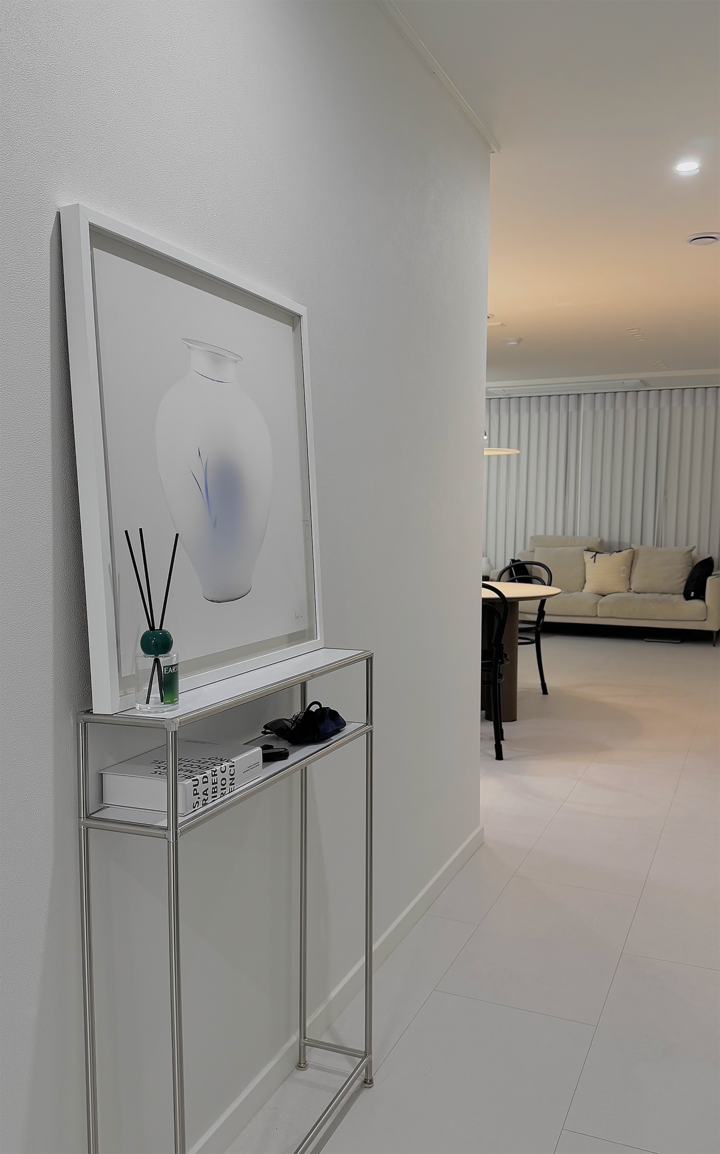 白と青のトーンのモダンな廊下のインテリア、スリムな棚に月の壺の額絵とディフューザーが配置された清潔感のある空間