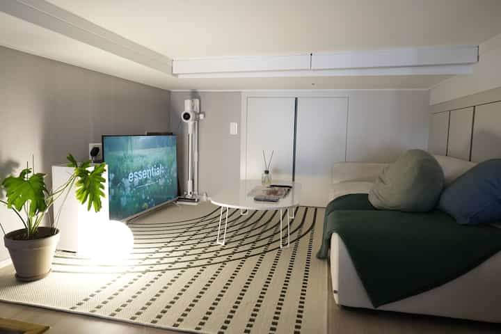 ナチュラルな色調のコンパクトなリビングルーム、ホワイトソファとパターンラグ、植物とテーブルランプが配置された雰囲気のあるインテリア