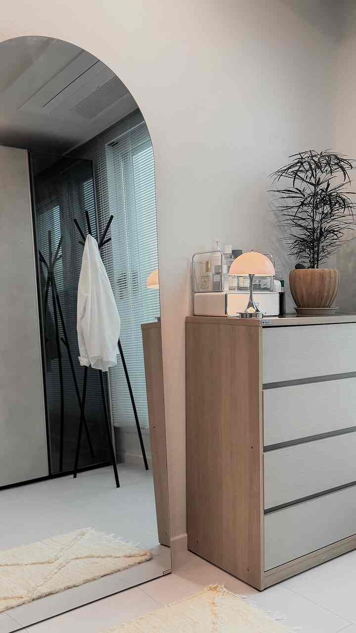 ベージュと白のトーンのウォークインクローゼット、ドレッサーと大型の全身鏡、植物とテーブルランプが配置された清潔感のあるモダンな空間