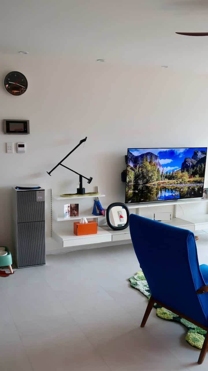 白と青のトーンのリビング、テレビ台と青いアームチェア、犬用グッズが配置されたすっきりとしたモダンなインテリア