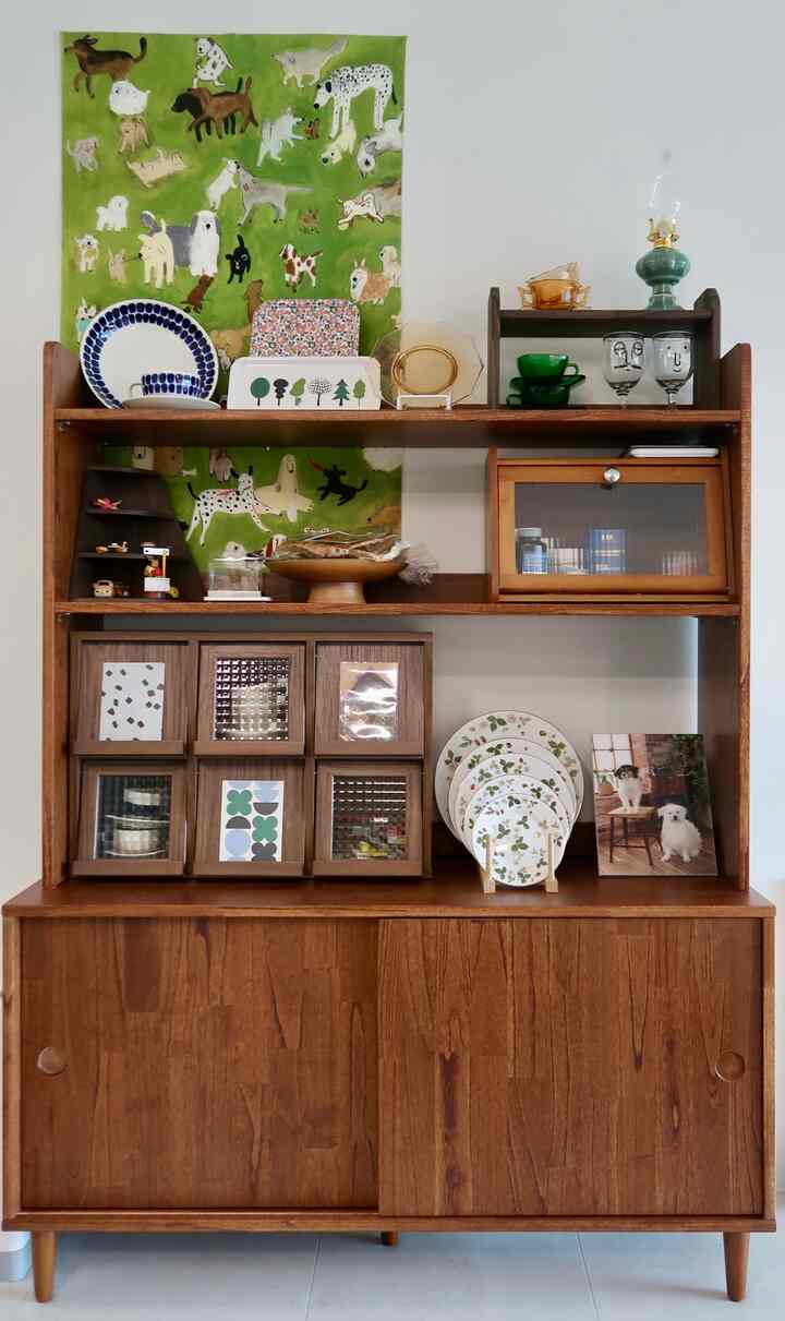 温かみのあるブラウンウッドトーンの収納棚が印象的な、犬のテーマの緑色ファブリックポスターが壁に飾られた雰囲気のあるインテリア