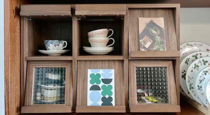 ナチュラルな木目調のキャビネットにヴィンテージのティーカップと皿が配置された、温かみのある雰囲気のあるインテリア