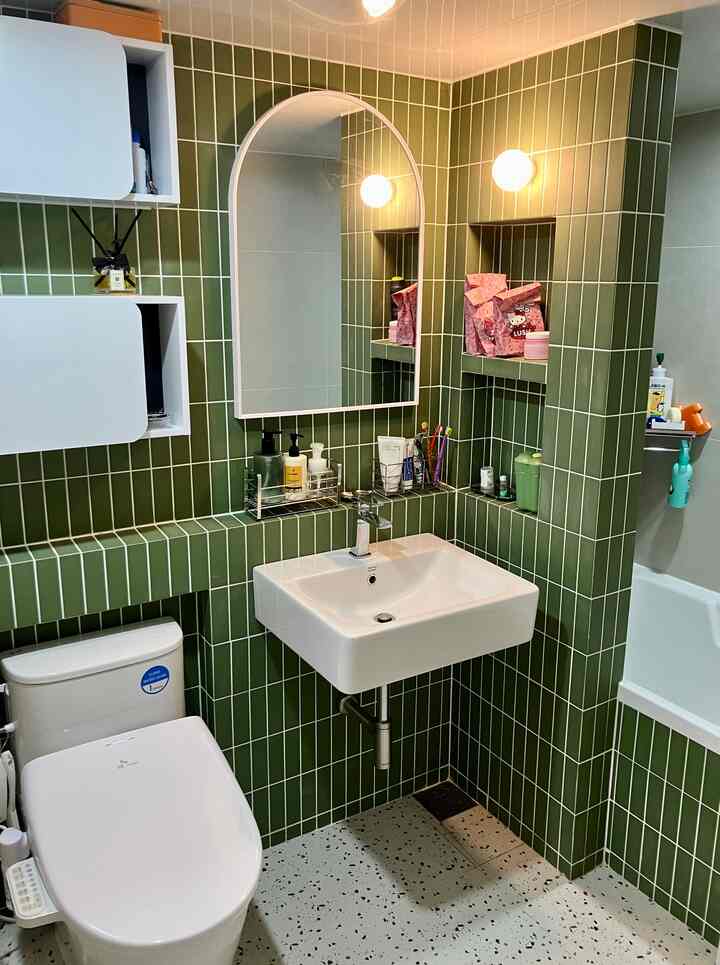 緑色のタイル壁と白い洗面台、トイレ、浴槽がある小さなバスルーム空間