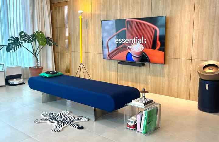 ブルーのベンチソファと木目調の壁が調和するリビング、壁掛け大型テレビとミニマルな小物が印象的な自然なモダンなインテリア