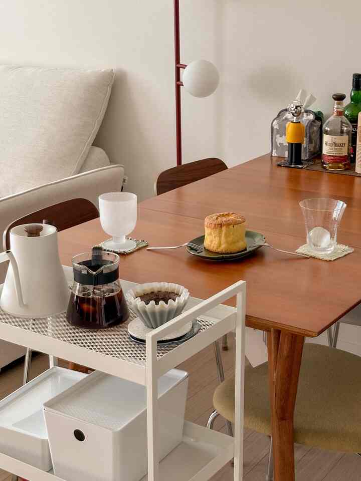 白と木目調が調和したミッドセンチュリーモダンのダイニング、食卓にホームカフェのアイテムとワゴンが配置された雰囲気のある空間
