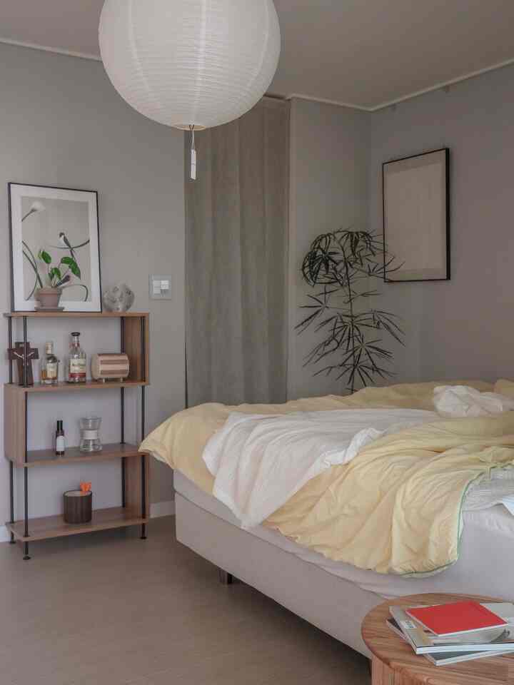 グレーのトーンで黄色い寝具とナチュラルな木製棚、植物が配置されたモダンな寝室