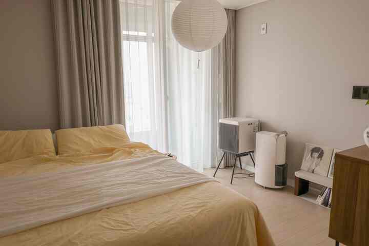 グレーの壁と黄色の寝具が調和した寝室、和紙のペンダントライトと遮光カーテンが配置された落ち着いた空間