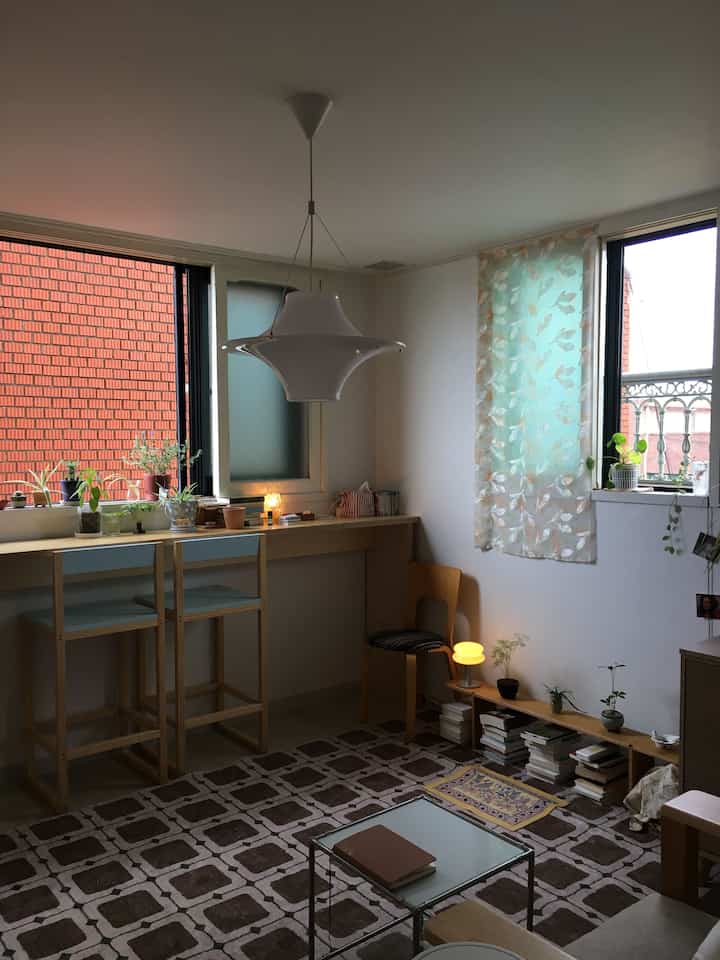 ナチュラルな色調の狭いリビングルーム、窓際にデスクと植物が配置されたシンプルで落ち着いたインテリア