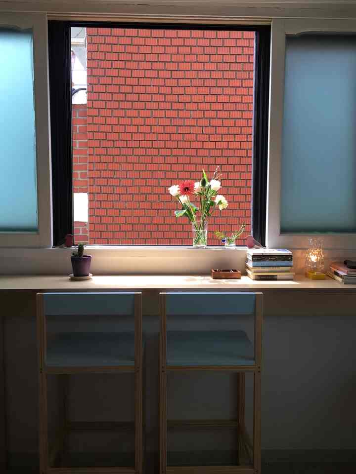 スカイブルーと白を基調としたカウンターテーブルとカウンタースツールが窓際に配置された、ミニマルで明るい雰囲気の空間