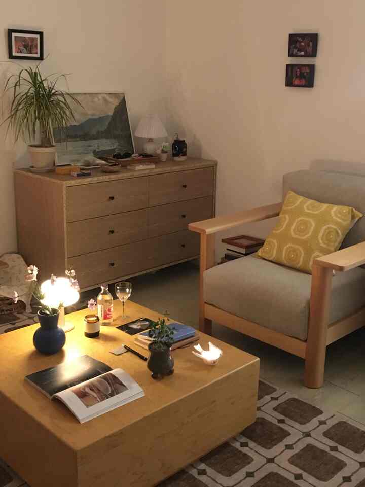 暖かいベージュと木目調のリビング、木製のドレッサーと黄色のクッションがあるアームチェアが落ち着いた雰囲気を醸し出す空間