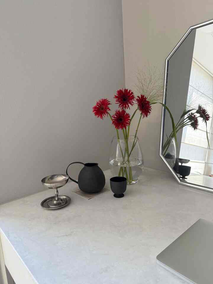 柔らかなニュートラルトーンの壁と大理石の天板に透明な花瓶と鮮やかな赤い花、黒い急須とティーカップが配置されたモダンで自然な雰囲気の化粧台空間