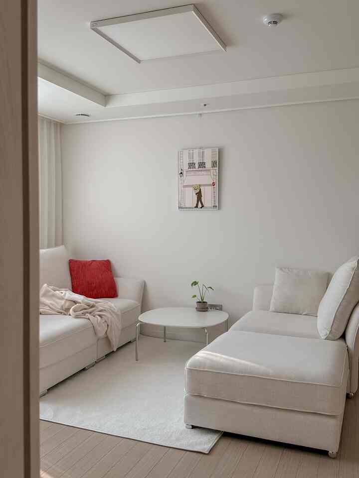 白とナチュラルトーンの調和した4人用リビング、モジュラーソファと丸いコーヒーテーブルが配置されたすっきりとした空間