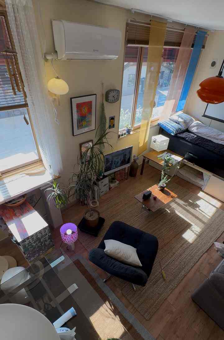 明るいアイボリー色の壁と木目調の床が特徴の寝室、ミッドセンチュリーモダンスタイルのアームチェアとオレンジのペンダントライトが調和した印象的な空間