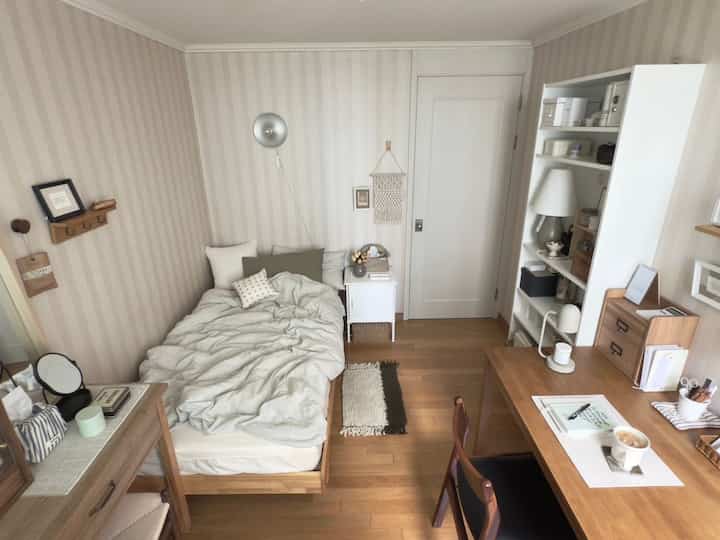 温かみのあるナチュラルな木目調とホワイトのワンルーム、ベッドとデスク、収納が配置された落ち着いた空間