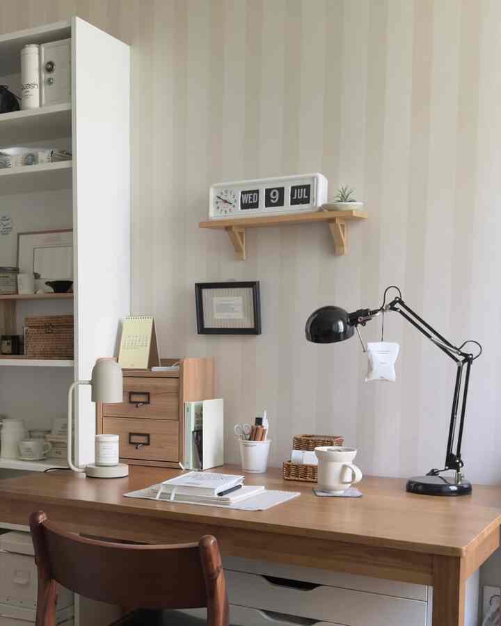 ナチュラルな木目調とホワイト、ブラックのアクセントがあるホームオフィス、木製デスクや照明、壁の額縁が配置された整った作業スペース