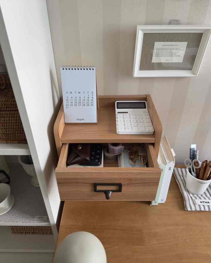木目調のチェストと机の上にカレンダーや計算機などのアクセサリーが配置されたシンプルなホームオフィス空間