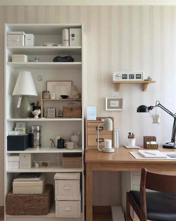 ベージュの壁紙とナチュラルな木製デスクがあるコンパクトなホームオフィス、整理整頓されたBILLYの6段本棚と収納ボックスが配置された雰囲気あるインテリア