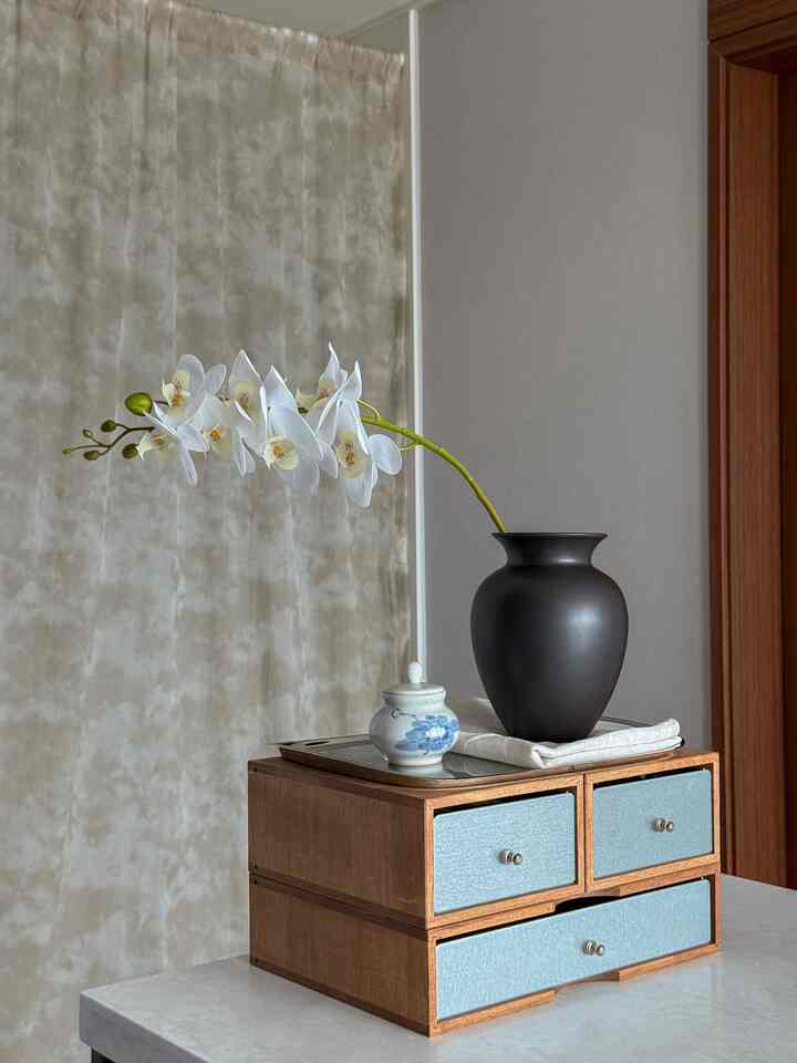 ナチュラルな木目調とベージュのカーテン背景のキッチンアイランド、黒い花瓶と白い胡蝶蘭が配置されたモダンで雰囲気のあるインテリア