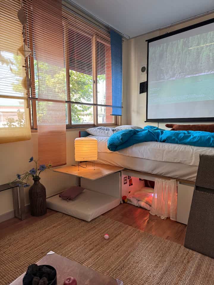 ナチュラルなベージュとブルーのトーンが調和したワンルーム、ベッド下に猫用のミニルームとDIY家具があるヴィンテージスタイルの空間