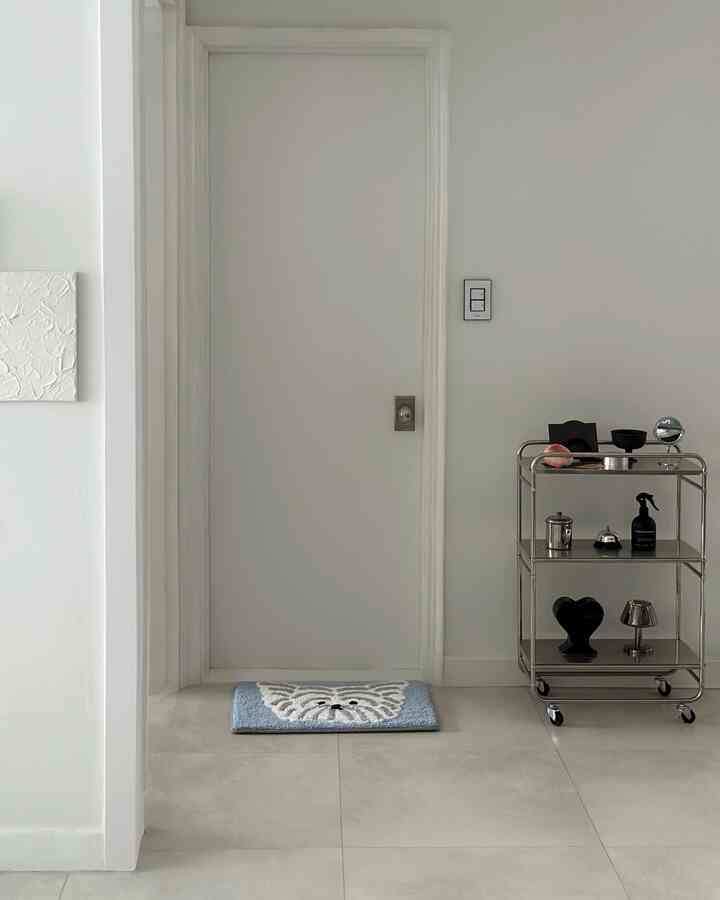 白とグレーのトーンの玄関、青と白のパターンのラグとステンレス製ワゴンがミニマルに配置された清潔感のあるインテリア