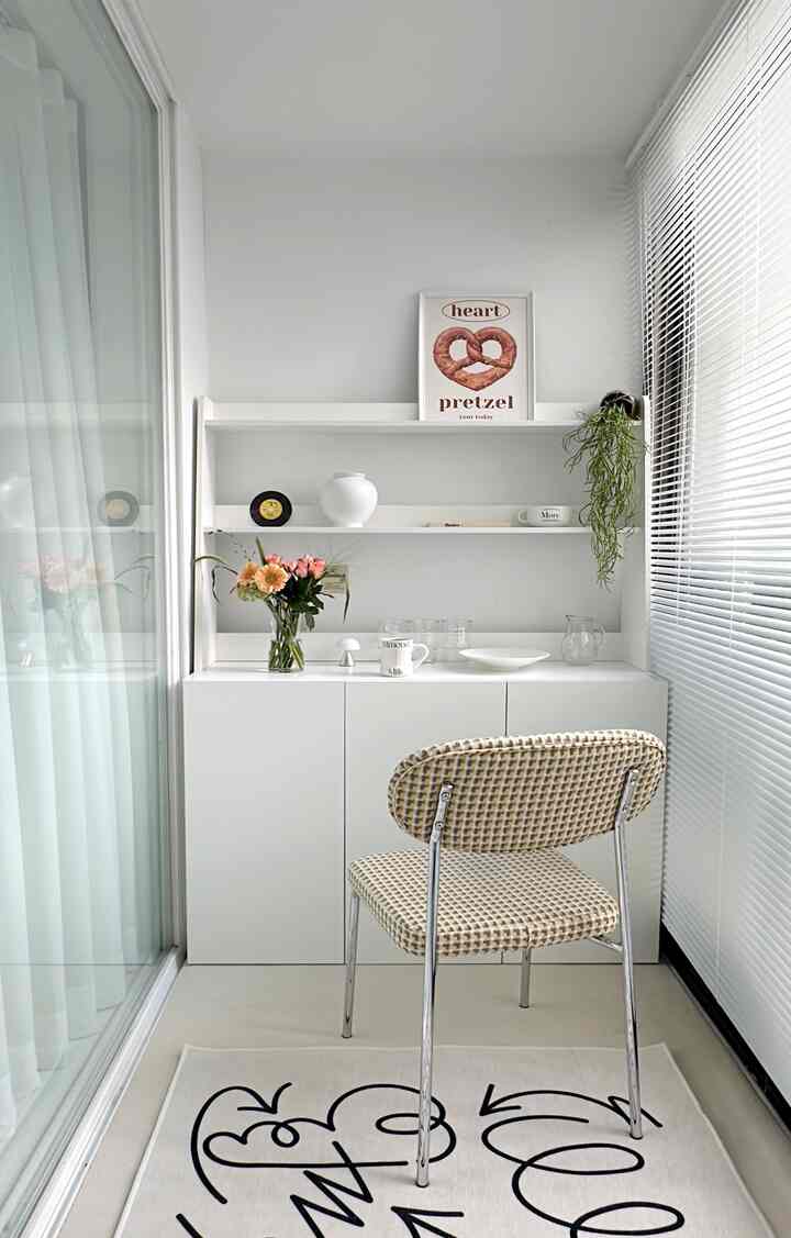白を基調としたベランダ、白い収納キャビネットとダイニングチェア、カフェ風のポスターと花が置かれた雰囲気のあるおうちカフェ空間