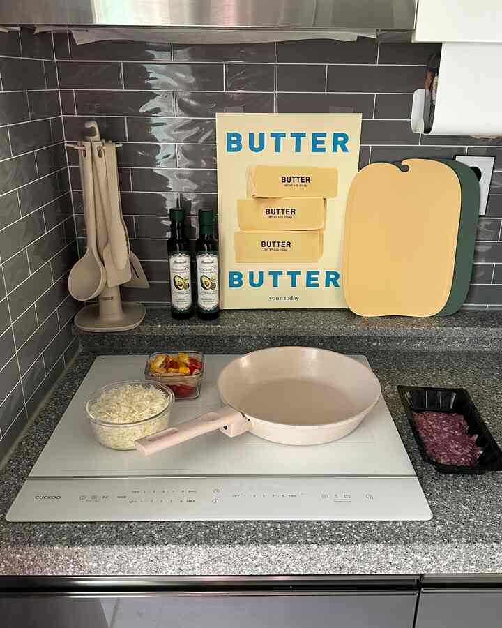 グレーのタイル壁とベージュの調理器具、ピンクのフライパンが置かれたキッチンのインテリア