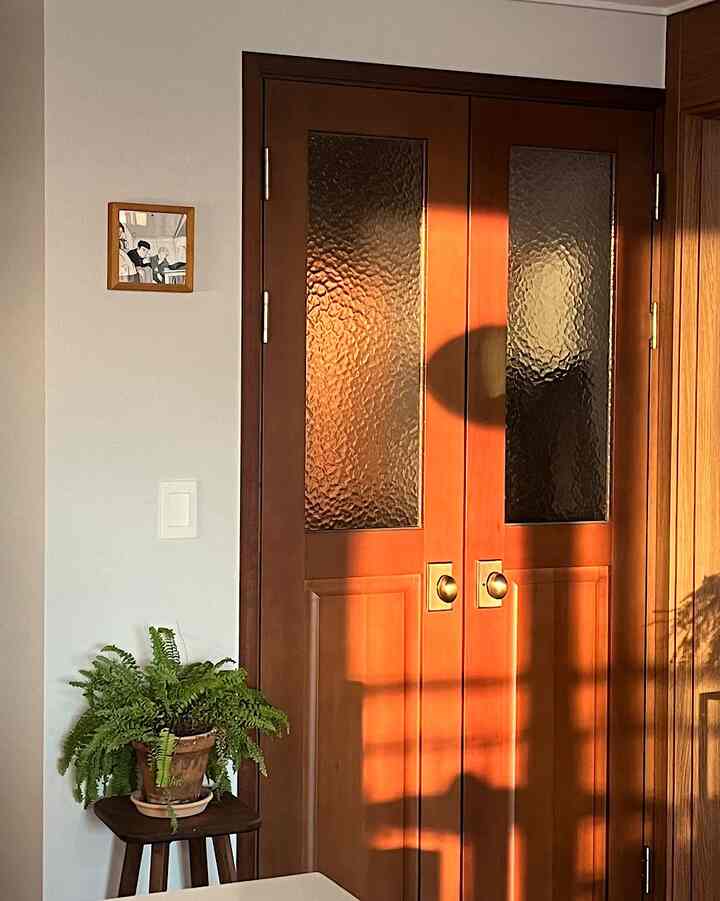 ナチュラルな木目調の玄関、緑の植物が置かれた小さな木製スツールと中くらいの木製ドアが配置された雰囲気のある空間