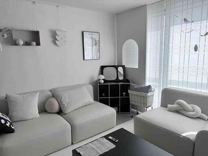 モノトーンのリビングルーム、モジュラーソファとシンプルなブラック家具、ホワイトブラインドが配置された洗練された空間