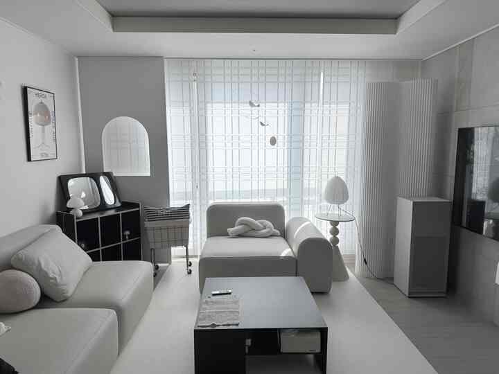 明るいホワイトトーンの横長リビング、ホワイトソファとブラックのコーヒーテーブル、ZENスタイルのブラインドとモビールが調和したインテリア